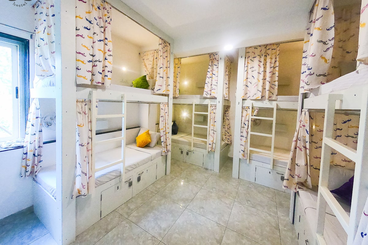A hostel room with bunk beds, numbered storage compartments, and patterned curtains.