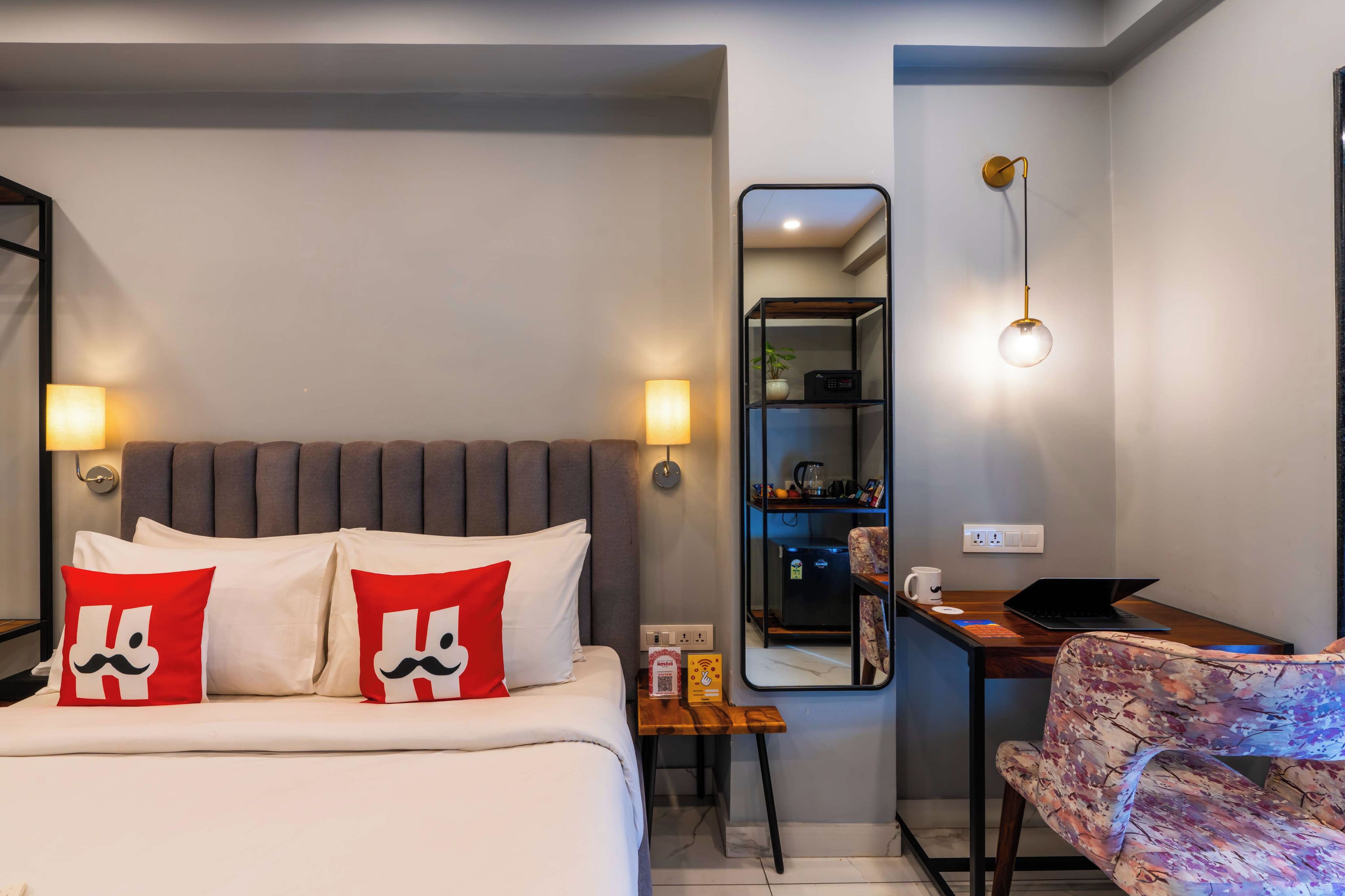 Une chambre d’hôtel équipée d’un lit, d’un bureau, d’une chaise, d’un miroir et d’un luminaire fixé au mur.