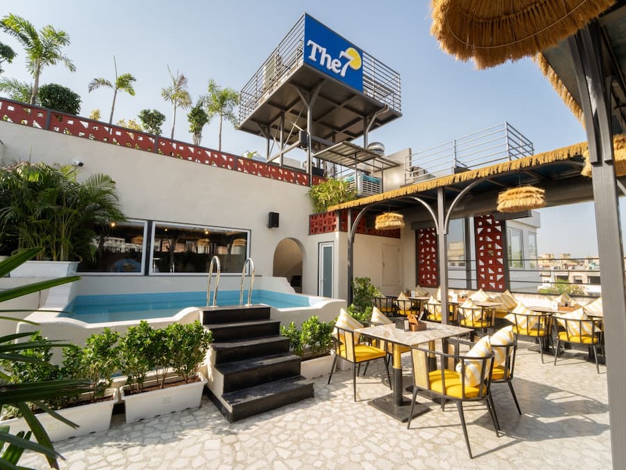 A rooftop pool area with outdoor seating and a sign for 'The7'.