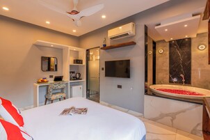 Quarto de hotel moderno com uma cama, escrivaninha com um laptop, televisão e chuveiro com paredes de mármore, além de ar-condicionado.