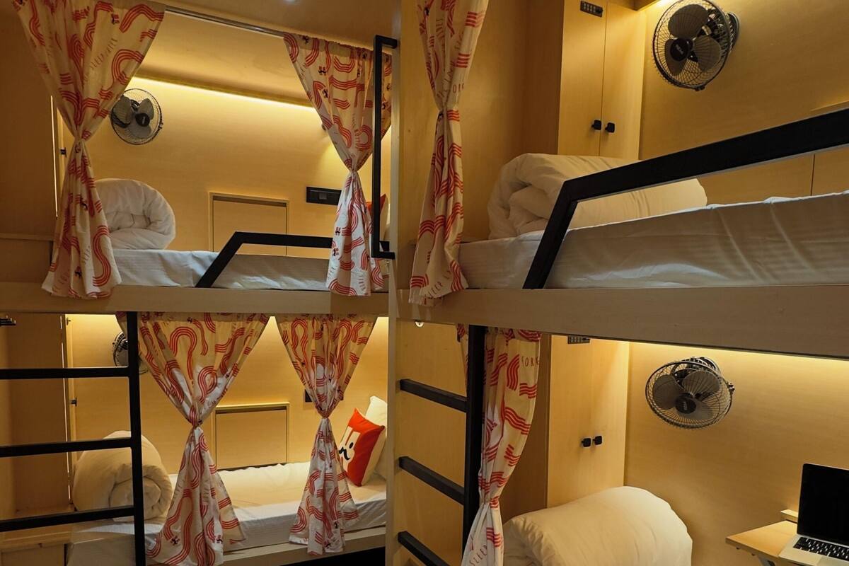 A bunk bed room with a carpeted floor, a desk with a laptop, and a wall-mounted fan.