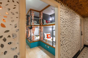 Quarto de hotel com beliche, pequeno espaço de cozinha e banheiro com vaso sanitário e pia.