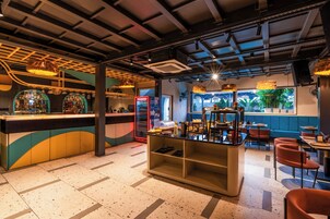 Un'area bar con un bancone, scaffali pieni di bottiglie e un frigorifero. Sono presenti zone con tavoli e sedie.