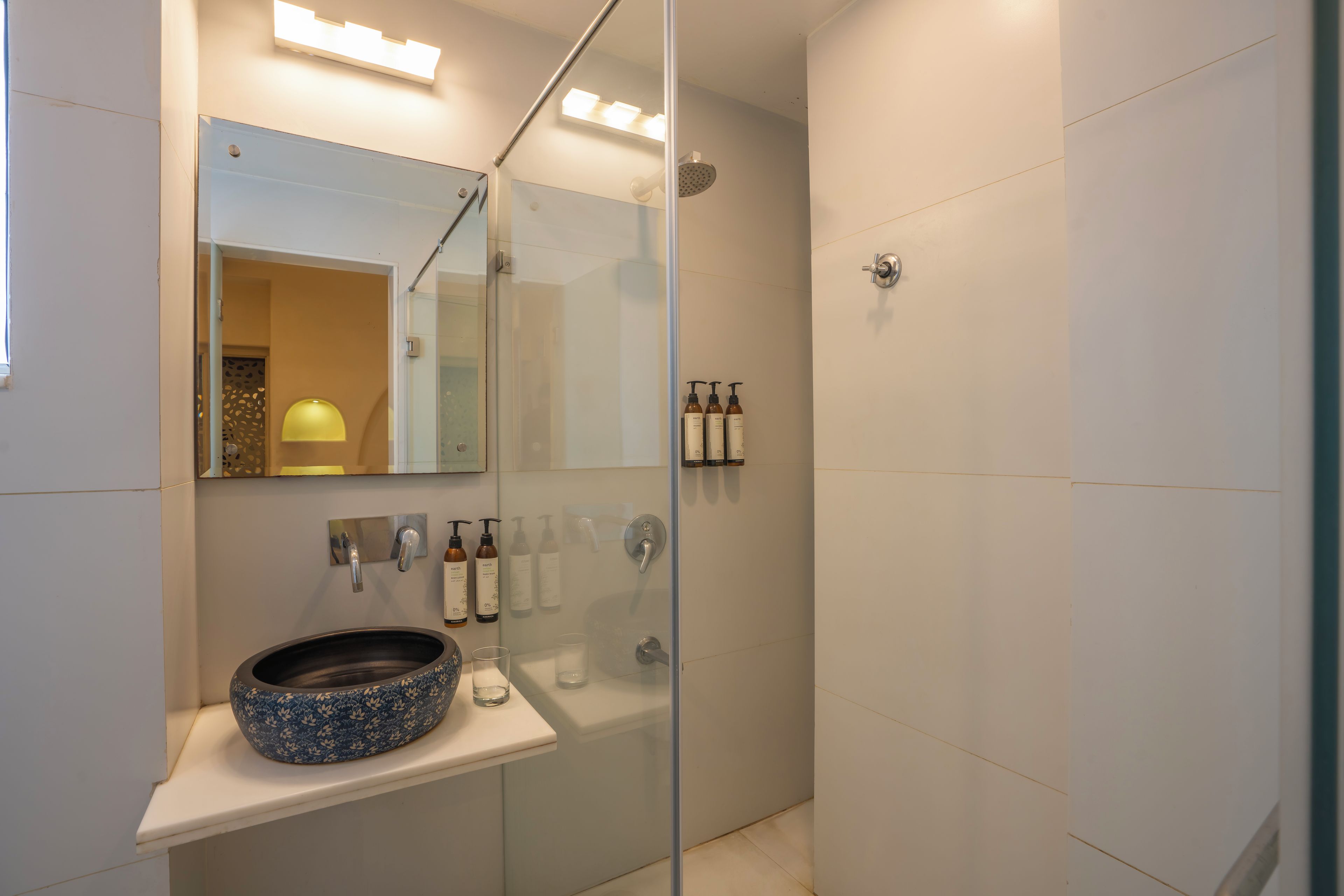 Un baño moderno con ducha envuelta en vidrio, un lavabo con un recipiente decorativo y un espejo sobre el lavabo.