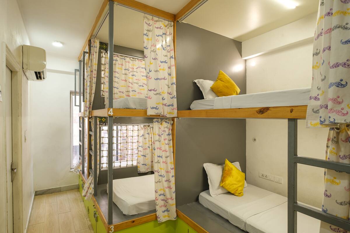 A dormitory room with bunk beds, a window with a curtain, and an air conditioning unit.