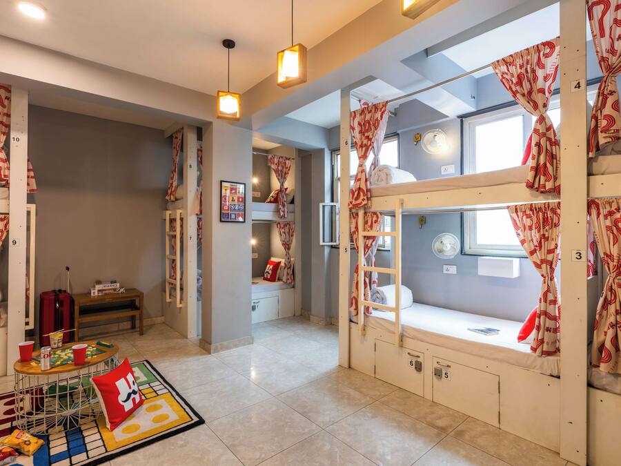Habitación de hotel con literas, una mesita con un juego de mesa, un ventilador y cortinas con estampado.