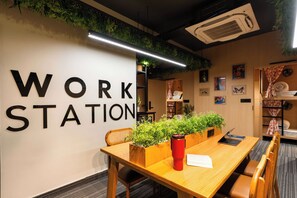 A work station area with a wooden table, chairs, a red water bottle, and a wall with the words 'WORK STATION' in large letters. - Moustache Jaipur (Jaipur)