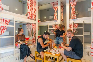 Quarto com beliches, uma mesa pequena e um grupo de pessoas jogando cartas.