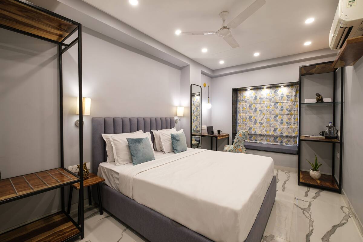 A modern bedroom with a large bed, bedside tables, a desk, a ceiling fan, and a window with patterned curtains.
