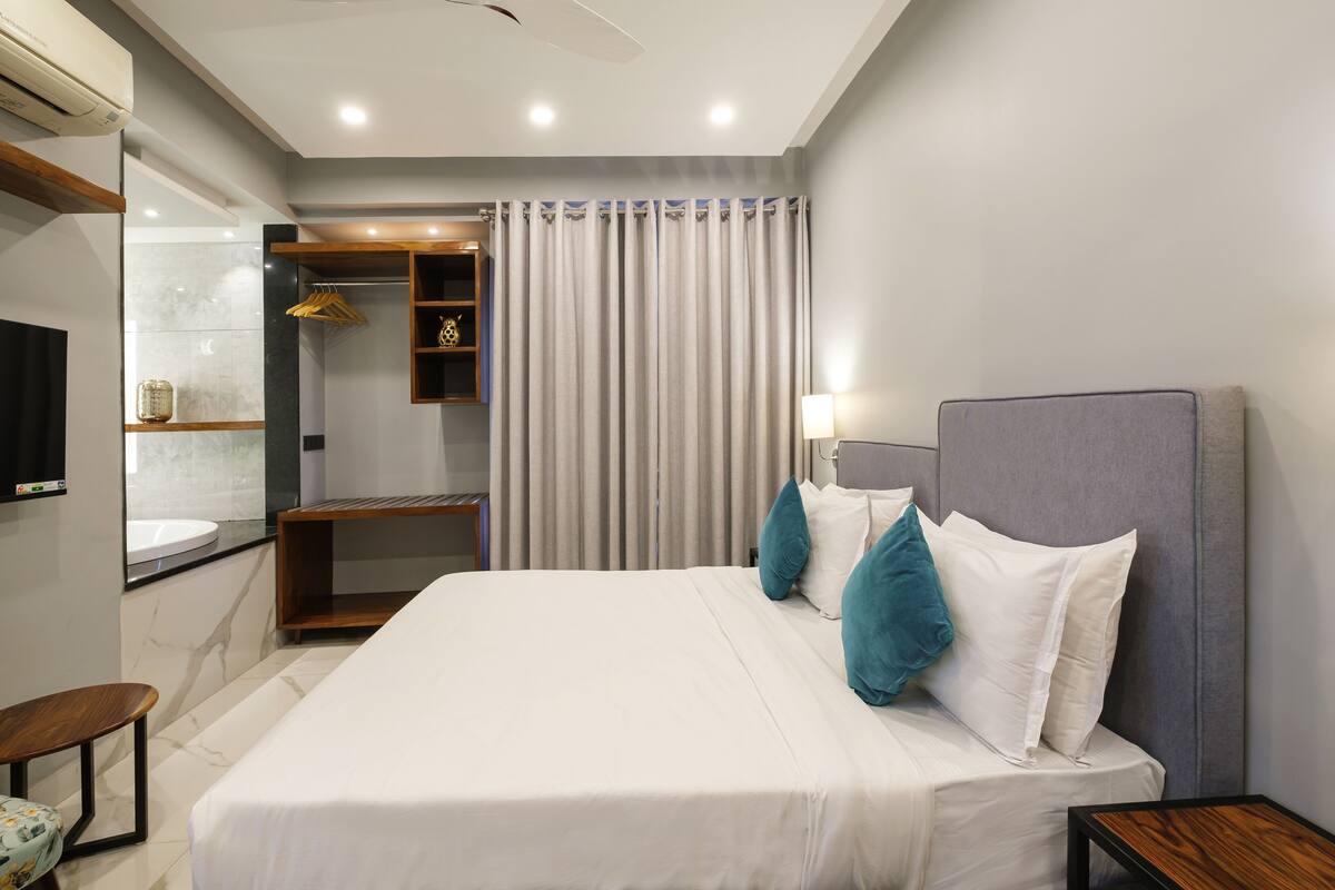 A modern hotel room with a large bed, a bedside table, a mirror, a wardrobe, and a TV.