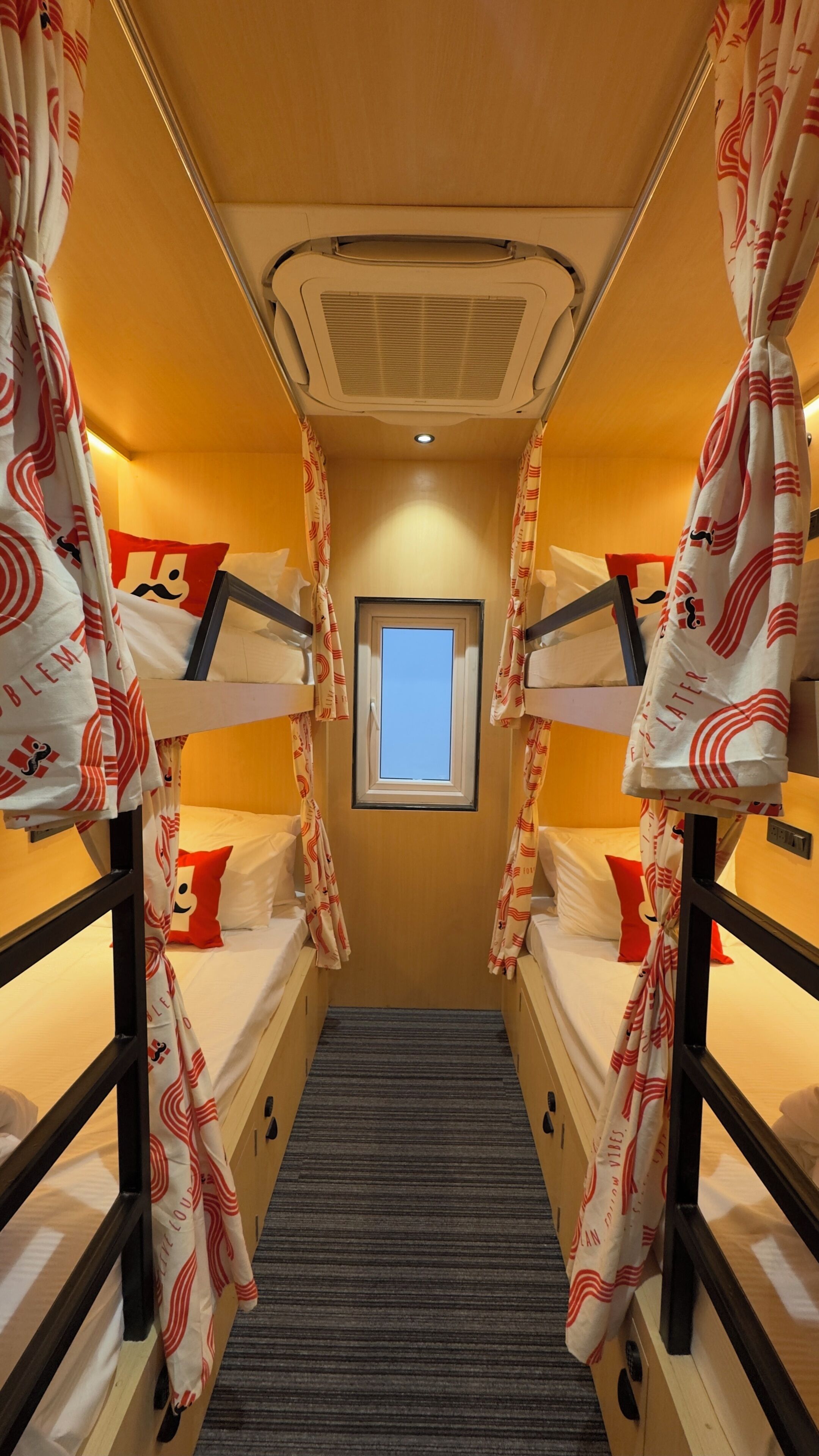 A narrow corridor with bunk beds, a window, and a ceiling vent.