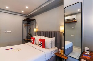Une chambre d’hôtel comprenant un lit, une table de chevet avec une lampe, un miroir et un climatiseur fixé au mur.