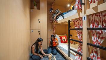 A bunk bed room with a game of Jenga. There are two people playing, a small plant on a shelf, and a suitcase on the floor.