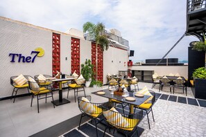 An outdoor seating area with tables and chairs, a wall with a sign, and a view of the cityscape. - Moustache Jaipur (Jaipur)
