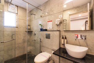 Casa de banho moderna com cabine de duche em vidro, sanita, lavatório e secador de cabelo fixado na parede.