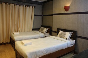 Una habitación de hotel con dos camas individuales, piso de madera, cortina y lámpara de pared.