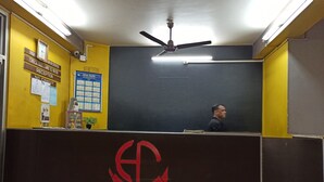 A reception area with a blackboard, a clock, and a logo on a brown counter. - Hotel Aane (Papumpare)