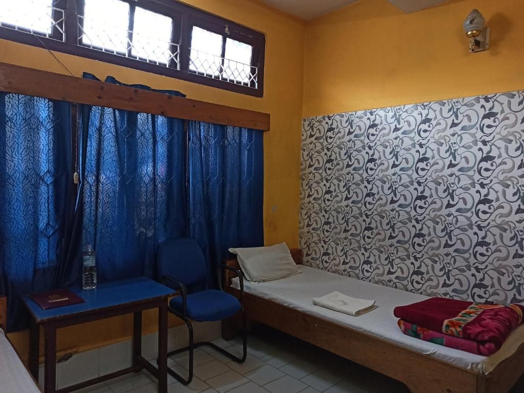 A small room with a single bed, a chair, a table, and a window with curtains.