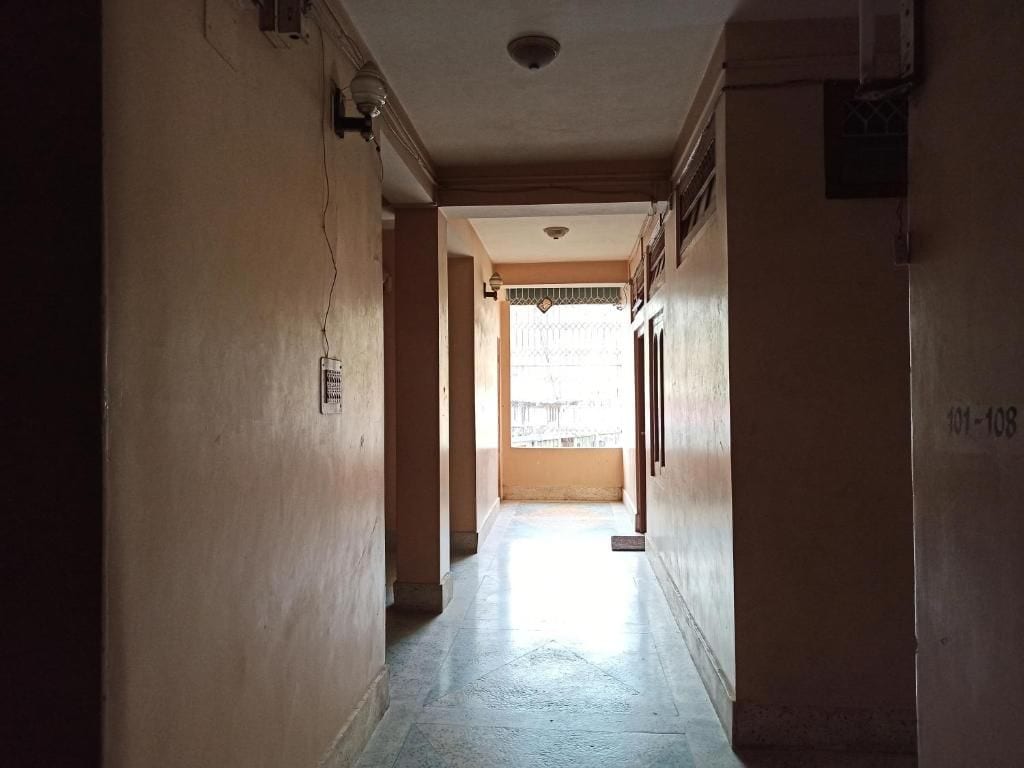 A corridor with a door at the end, a light fixture on the ceiling, and a wall-mounted electrical box.