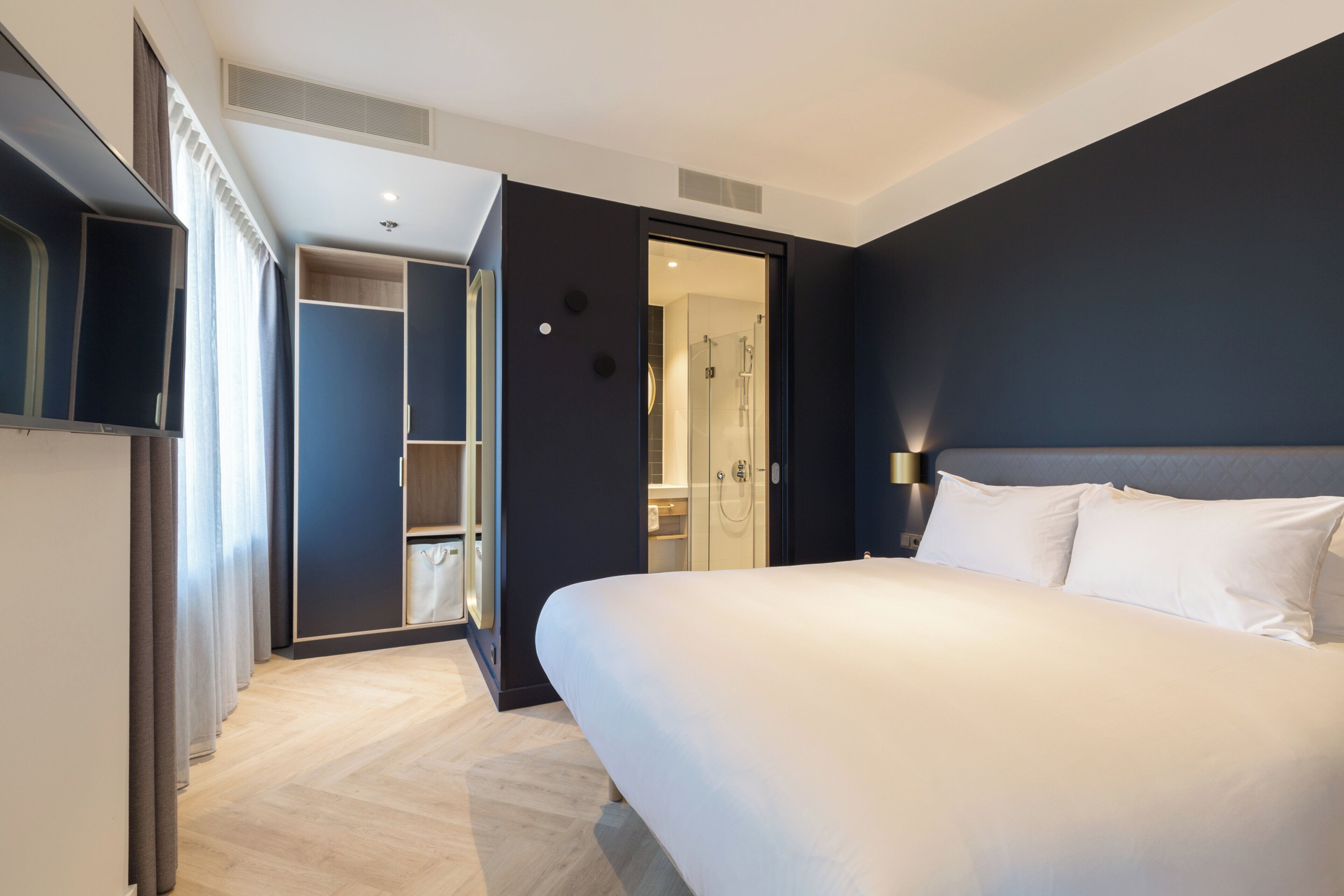 A modern hotel room with a large bed, a walk-in closet, and a shower area.