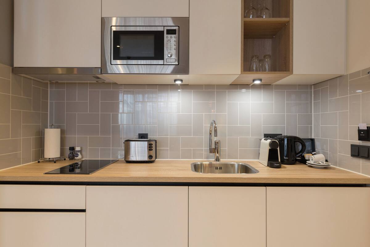 Een moderne keuken met een RVS magnetron, broodrooster, spoelbak en koffiezetapparaat.
