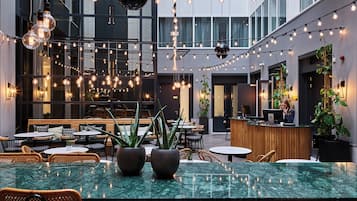 A modern indoor space with a central bar area, multiple seating arrangements, and hanging light fixtures.