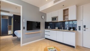 A modern kitchen with white cabinets, a microwave, and a coffee maker. There is a clock on the wall and a magazine on a table.