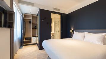 Een moderne hotelkamer met een groot bed, een inloopkast, een badkamer met een douchewand en uitzicht op de stad.
