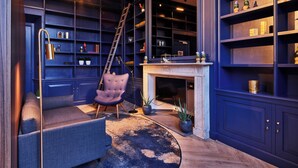 A room with a fireplace, a blue bookshelf, a purple armchair, and a ladder.