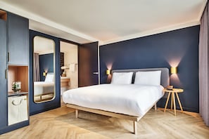 Una habitación de hotel moderna con una cama grande, mesitas de noche, un armario y un espejo.