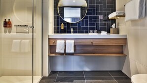 A modern bathroom with a glass-enclosed shower, a round mirror, and a dark tiled backsplash.