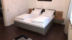 A neatly made bed with white linens, a wooden headboard, and a nightstand with a lamp. - Fachwerkhaus In Der Altstadt (Lueneburg)