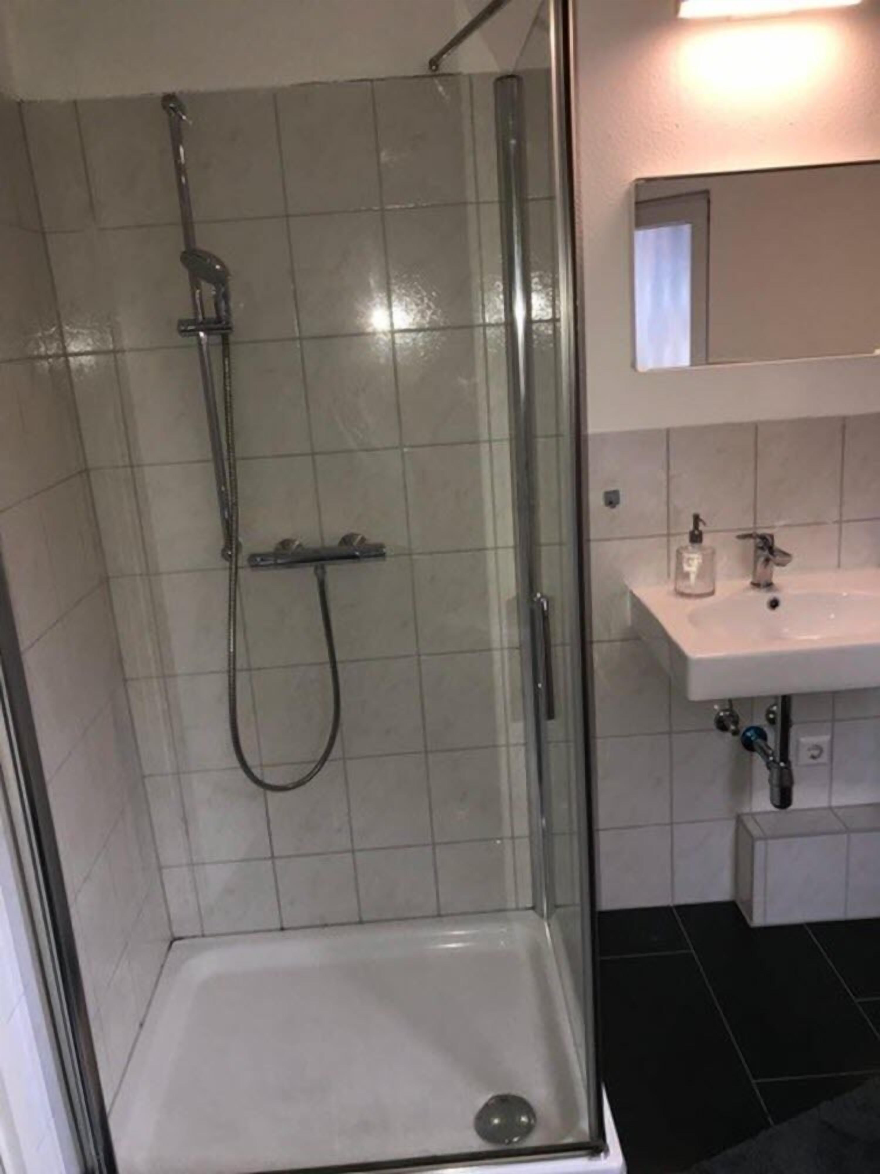 Una ducha con puerta de cristal, un lavamanos blanco y un espejo sobre él.