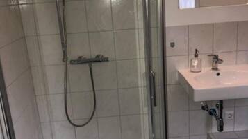 Une douche avec une porte en verre, un lavabo blanc et un miroir au-dessus du lavabo.