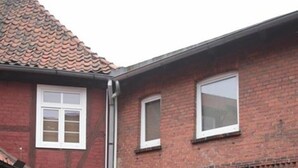 A two-story brick house with a front porch, a wooden bench, and a small garden area. - Fachwerkhaus In Der Altstadt (Lueneburg)