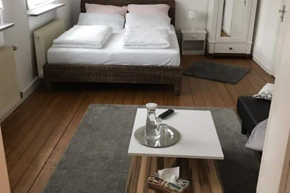 A bedroom with a bed, a bedside table, a small wooden table, a mirror, and a wardrobe.