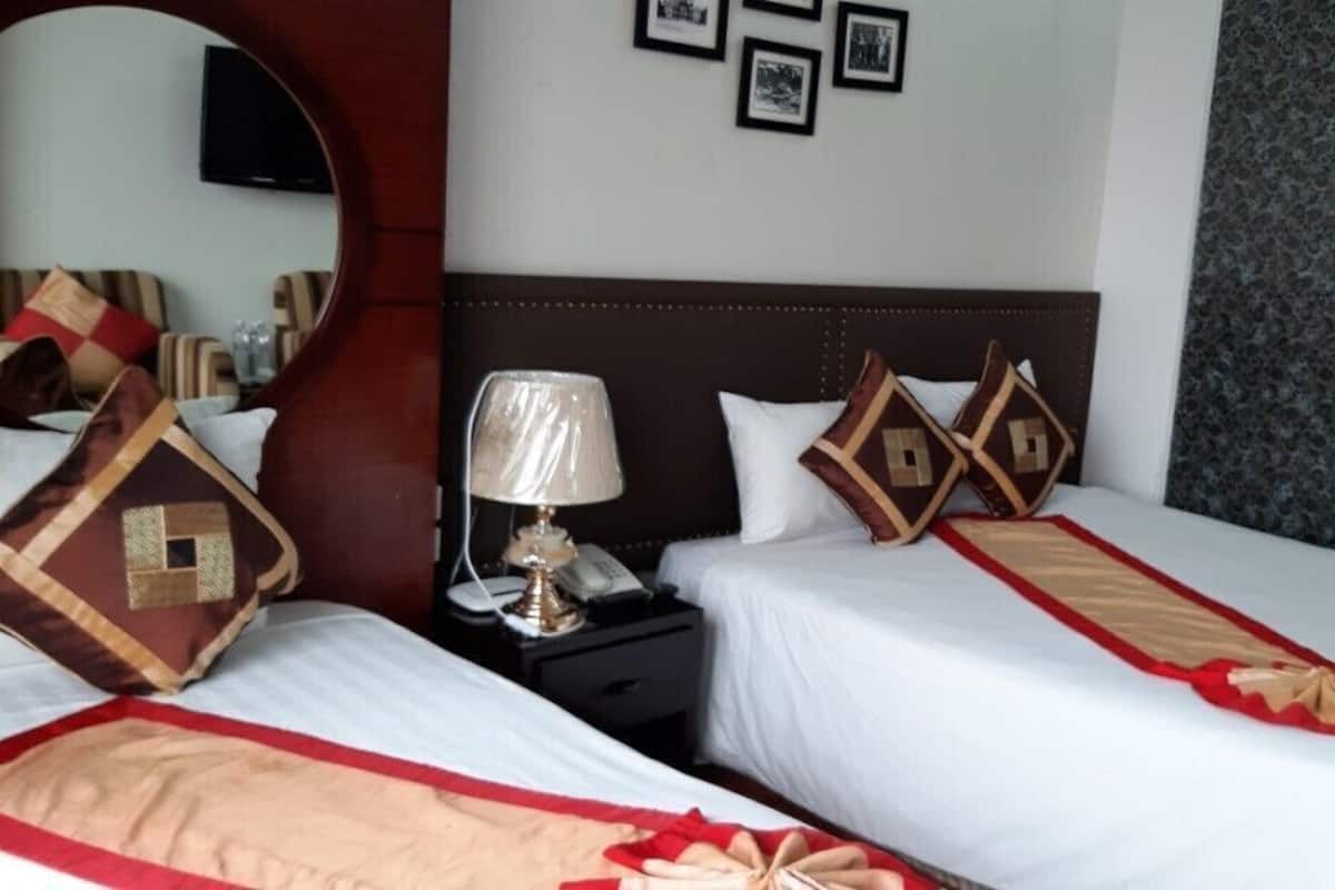 A hotel room with two beds, a nightstand with a lamp, a mirror, and framed pictures on the wall.