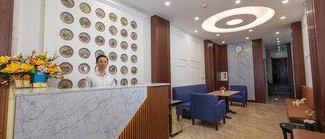 A hotel reception area with a marble counter, blue seating, and a wall decorated with plates.