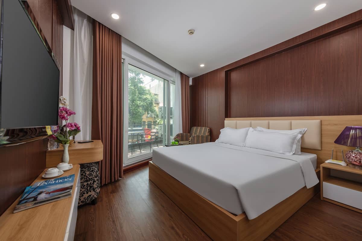 A modern hotel room with a large bed, wooden paneling, a glass door leading to an outdoor area, and a small table with a vase of flowers.