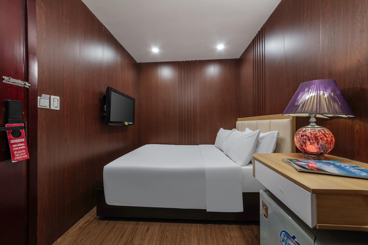 A hotel room with a bed, a television, a lamp, a desk, and a refrigerator.
