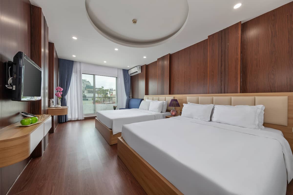 A hotel room with two beds, a TV, a small table with apples, and a window with curtains.