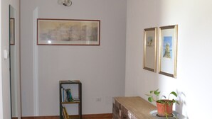 A hallway with a wooden floor, a wooden cabinet with drawers, a small bookshelf, and two framed pictures on the wall. - Cherry Season (Lanciano)