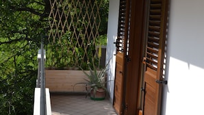 A balcony with a tiled floor, wooden shutters, and a potted plant. - Cherry Season (Lanciano)