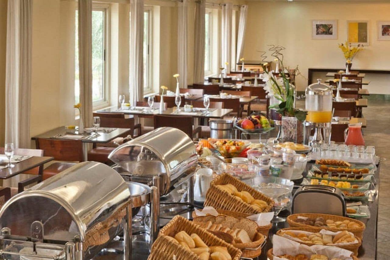 Uma mesa de buffet com diversos alimentos e bebidas, dispostos em mesas com cadeiras.
