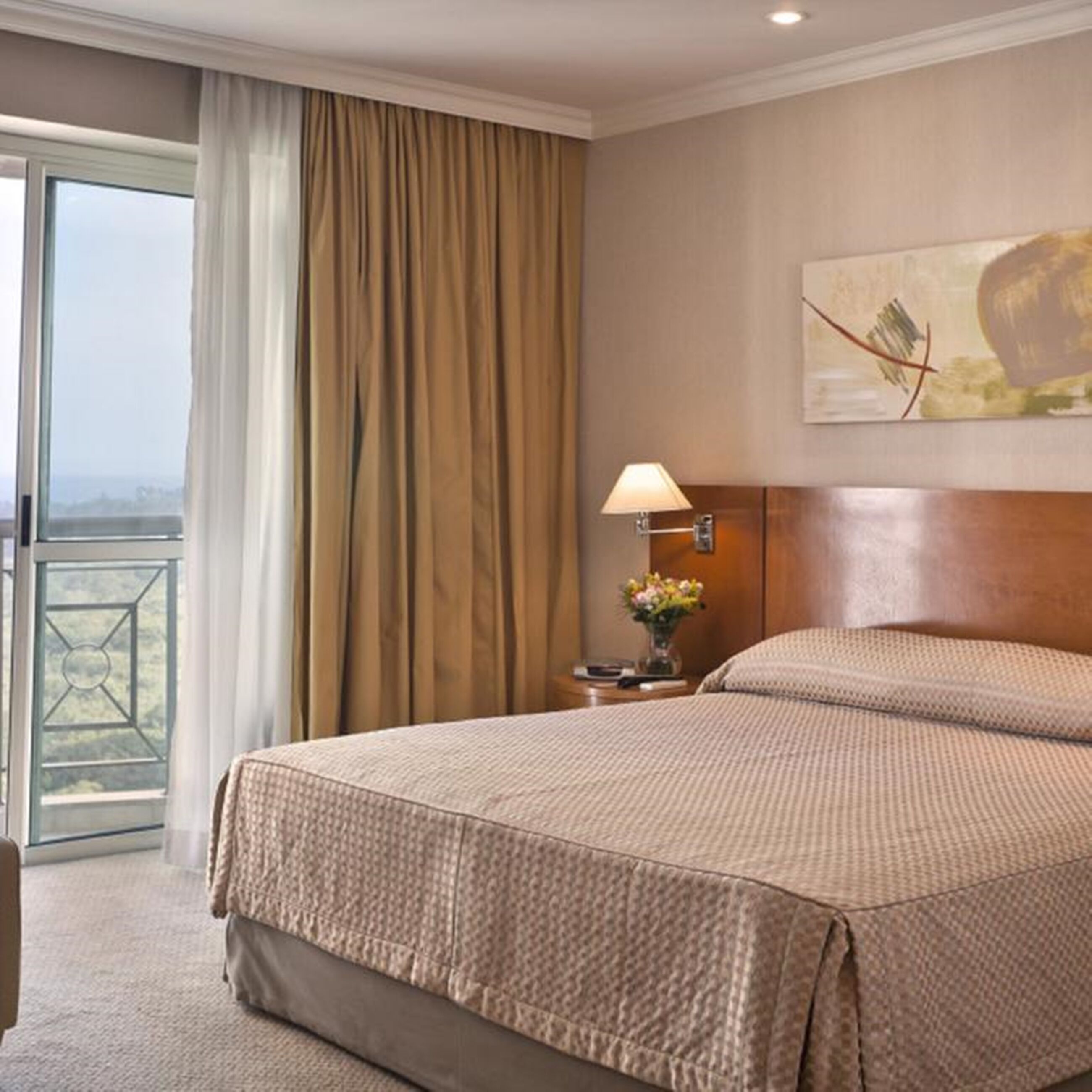 A hotel room with a large bed, a nightstand with a lamp, a painting on the wall, and a view through the window.