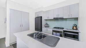 A modern kitchen with white cabinets, stainless steel appliances, and a built-in sink. - Accommodate Canberra - Dawes (Kingston)