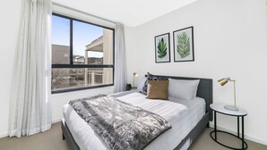 A modern bedroom with a large bed, a side table, and two framed leaf artworks on the wall. - Accommodate Canberra - Dawes (Kingston)