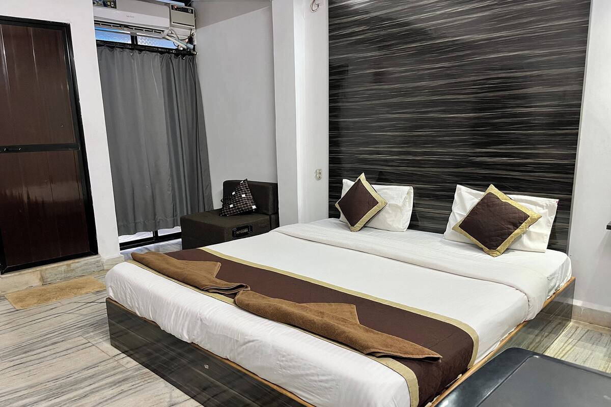 A hotel room with a large bed, a bedside table, a wardrobe, and a window with curtains.