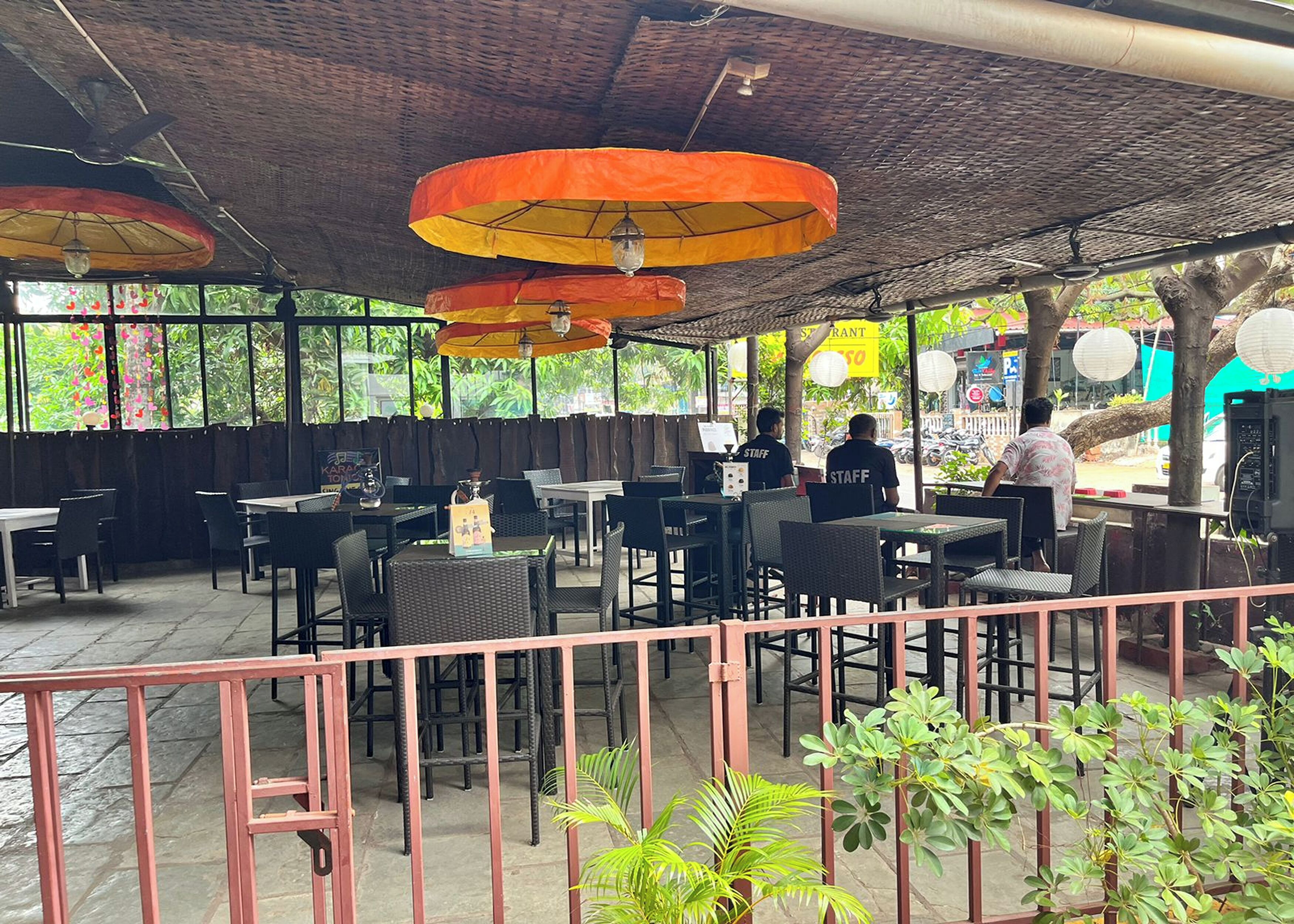 An outdoor restaurant with tables and chairs, covered by a roof with hanging lamps.