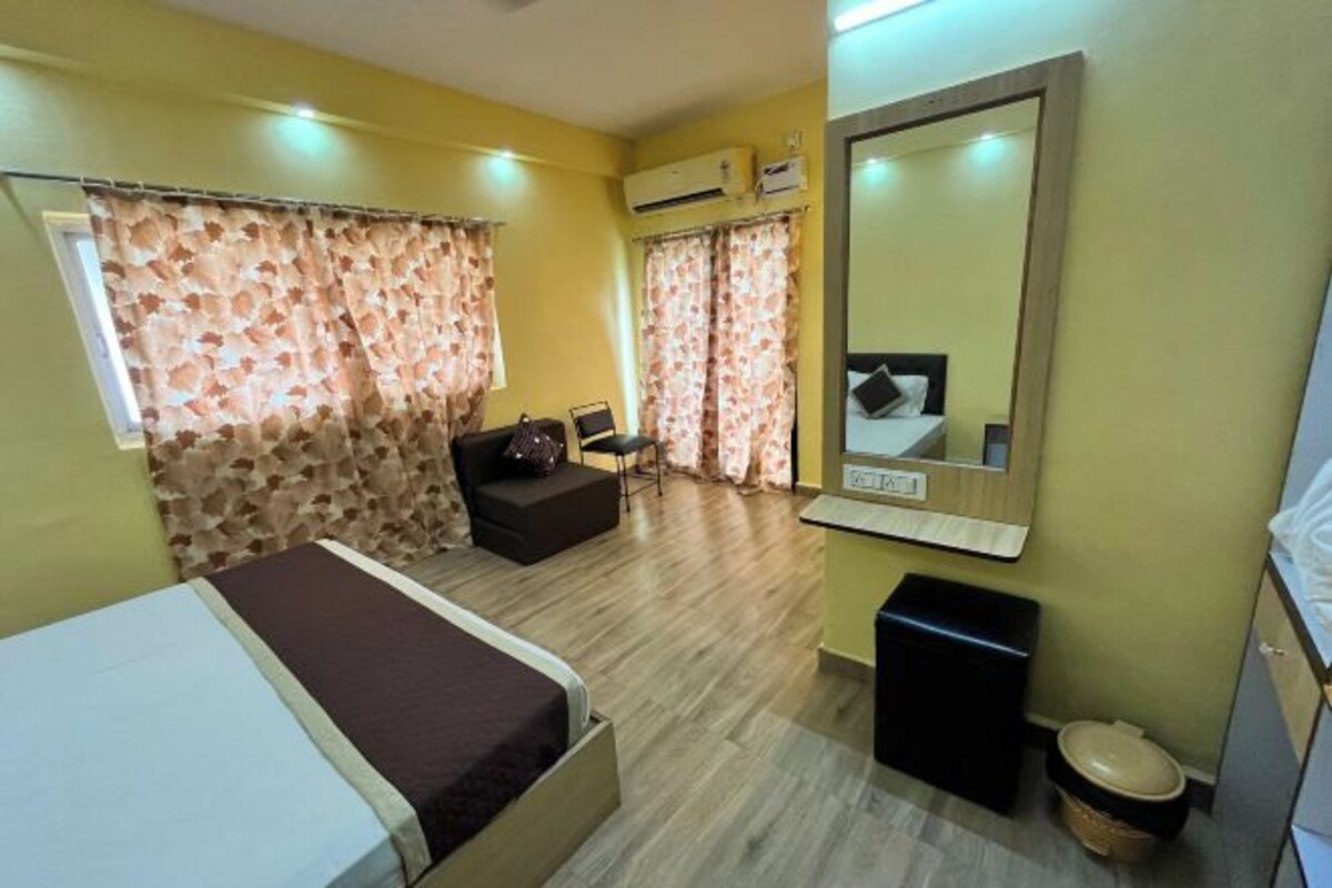 Une chambre d’hôtel avec un lit, un petit canapé, un bureau, un miroir et une poubelle.